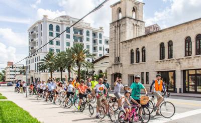 Group of cyclists wave in front of the Coral Gables Museum